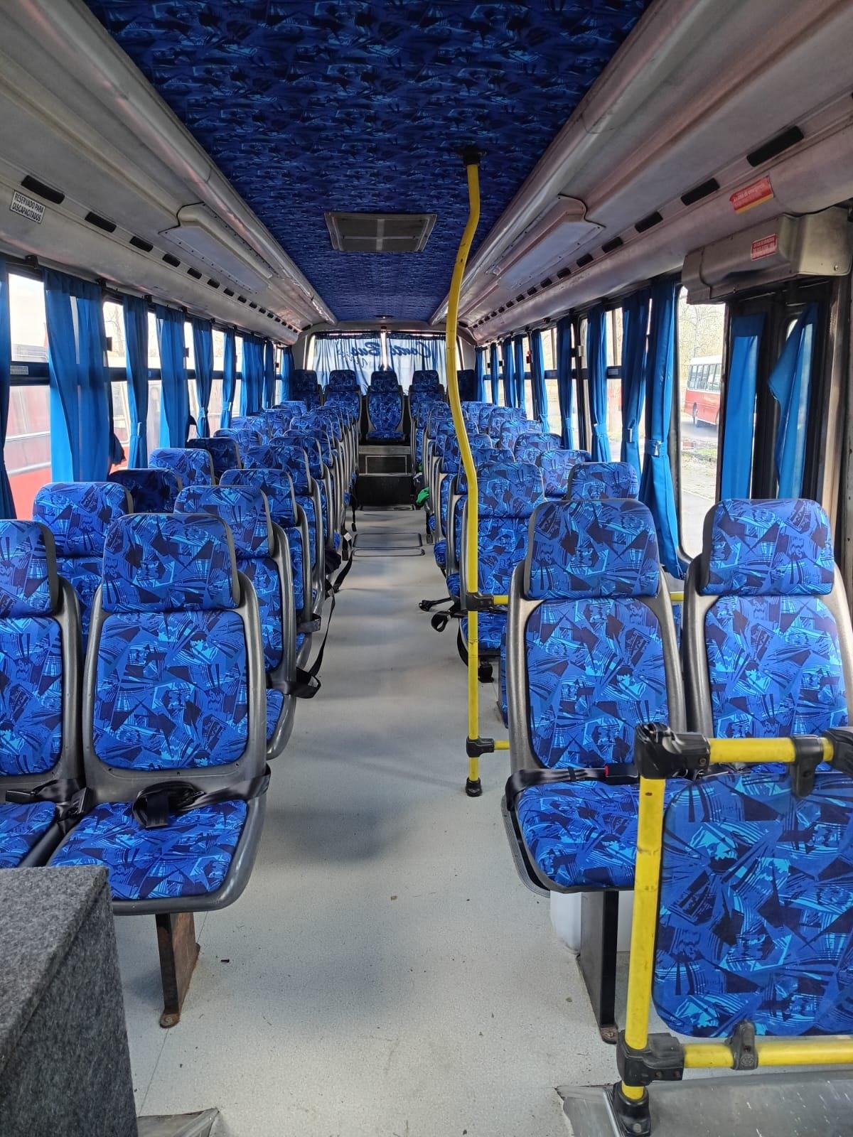 Interior de un micro con asientos tapizados en azul y cortinas celestes a lo largo del pasillo