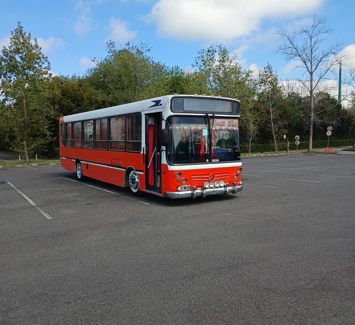 Micro rojo y blanco de Conti Bus con la puerta abierta en un estacionamiento rodeado de árboles
