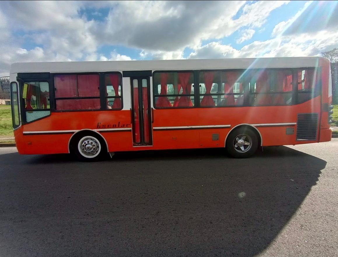 Micro escolar rojo de Conti Bus visto de costado, estacionado en una calle bajo el cielo nublado