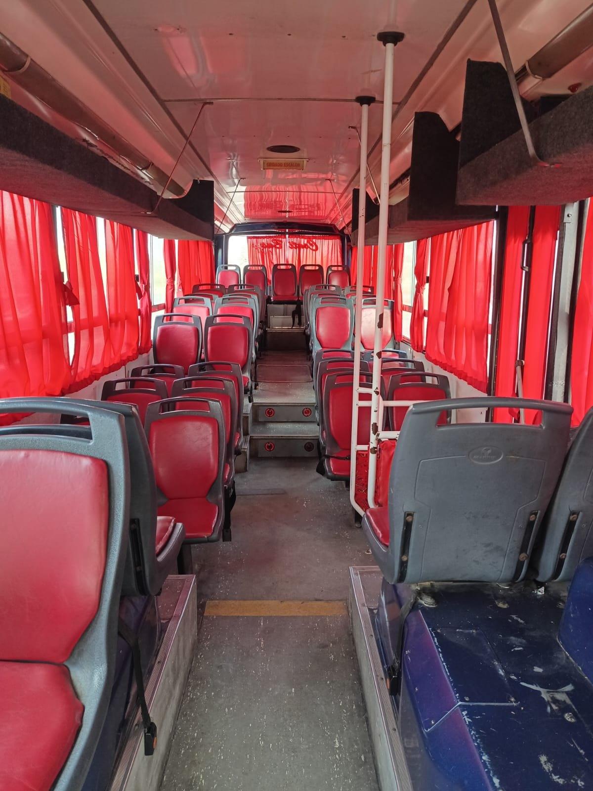 Interior de un micro con asientos y cortinas rojas a lo largo del pasillo
